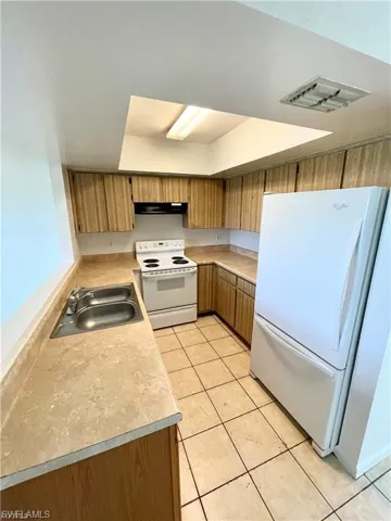 Kitchen featuring white appliances, brown cabinetry, light countertops, and light tile patterned floors