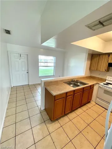 Kitchen featuring white electric range oven, brown cabinets, light countertops, and a peninsula