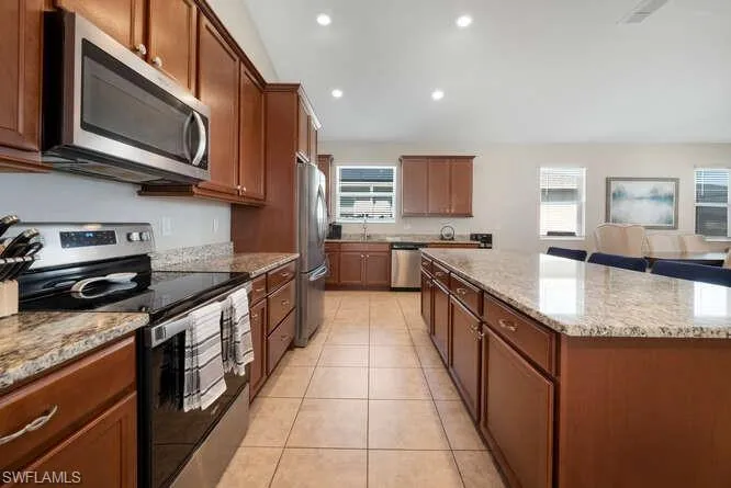 Kitchen with appliances with stainless steel finishes, a center island, light stone countertops, recessed lighting, and light tile patterned floors