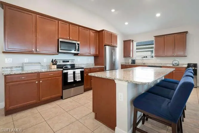 Kitchen featuring stainless steel appliances, light tile patterned floors, lofted ceiling, recessed lighting, and a kitchen island