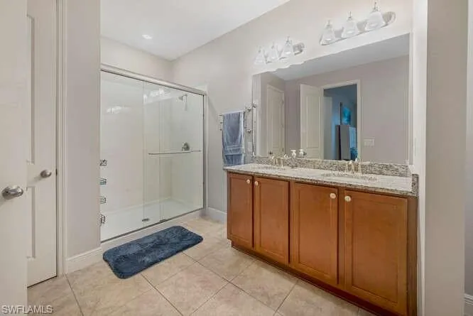 Bathroom with a shower stall, double vanity, and tile patterned flooring
