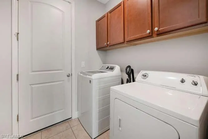 Laundry room with washer and clothes dryer, cabinet space, and light tile patterned floors
