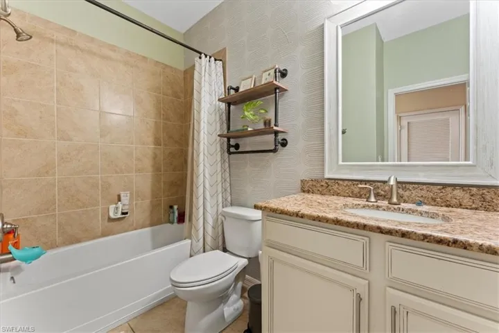 Bathroom featuring toilet, vanity, shower / tub combo with curtain, wallpapered walls, and tile patterned floors