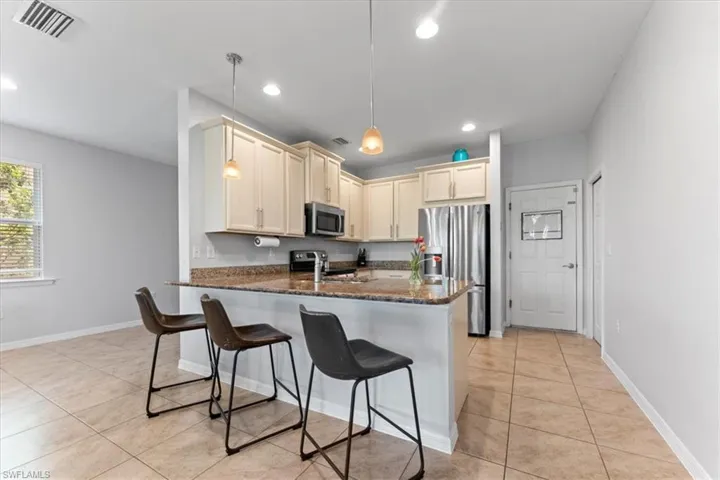 Kitchen with stainless steel appliances, a peninsula, light tile patterned flooring, dark stone counters, and a breakfast bar area