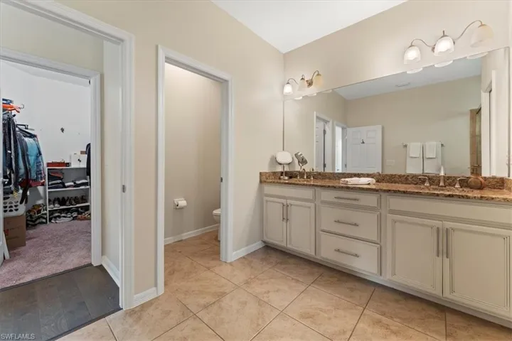 Full bathroom with double vanity, toilet, a walk in closet, and baseboards