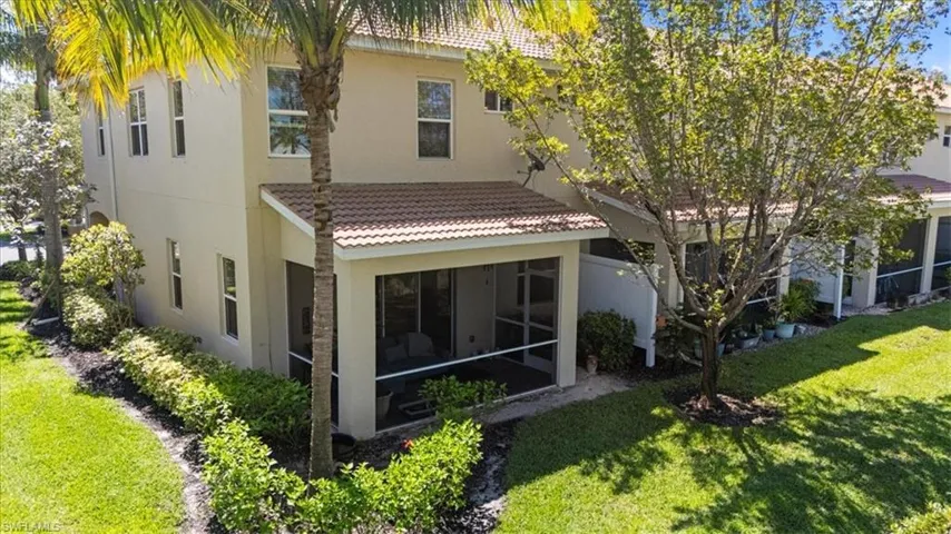 Rear view of house with a sunroom, stucco siding, a tile roof, and a lawn