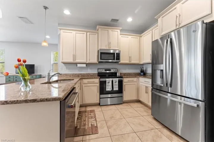 Kitchen featuring stainless steel appliances, a sink, a peninsula, light tile patterned flooring, and stone countertops