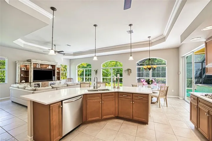 Kitchen featuring a ceiling fan, brown cabinets, a raised ceiling, pendant lighting, and ornamental molding