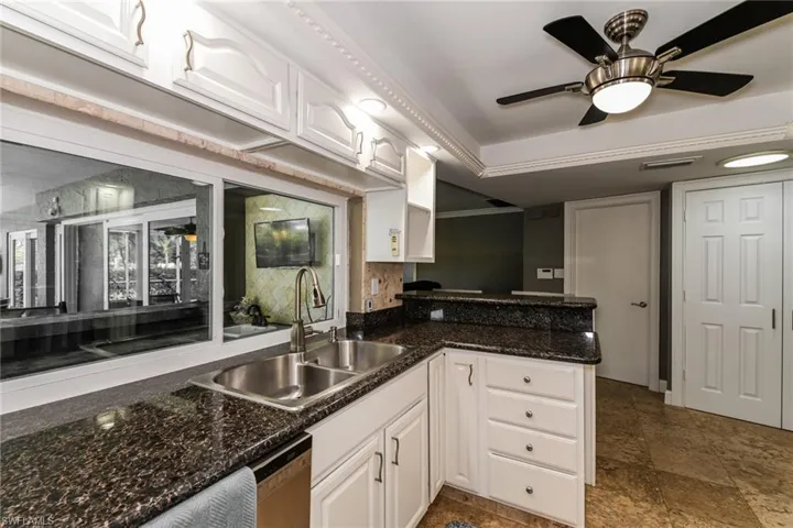 Kitchen featuring white cabinetry, a ceiling fan, a peninsula, dishwasher, and dark stone finish floors