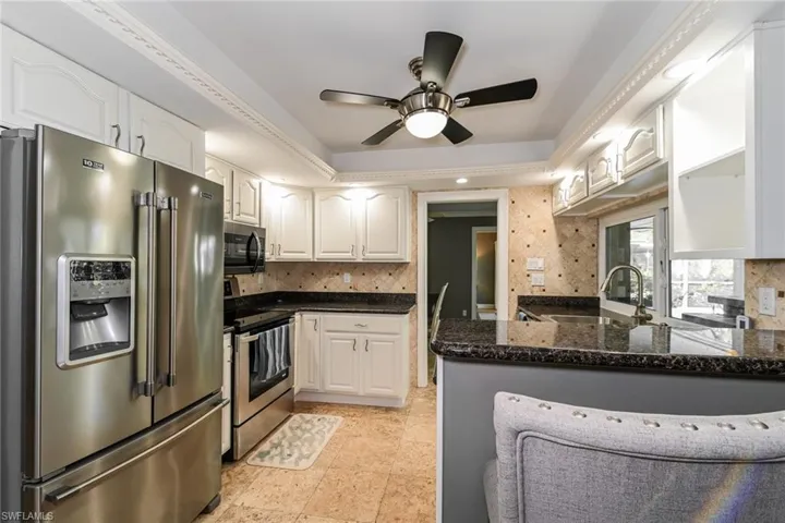 Kitchen with appliances with stainless steel finishes, ceiling fan, a peninsula, white cabinetry, and a raised ceiling