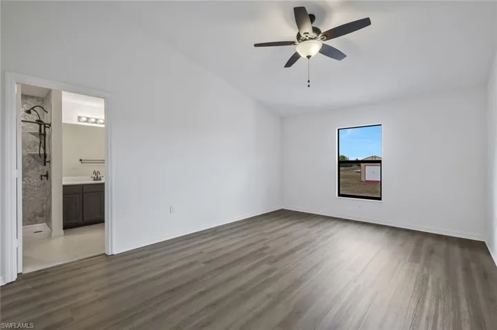 Unfurnished bedroom with vaulted ceiling, a ceiling fan, dark wood-type flooring, and ensuite bath