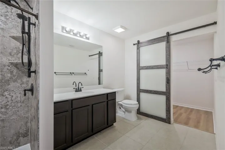 Full bath with vanity, a walk in closet, light tile patterned floors, and a stall shower