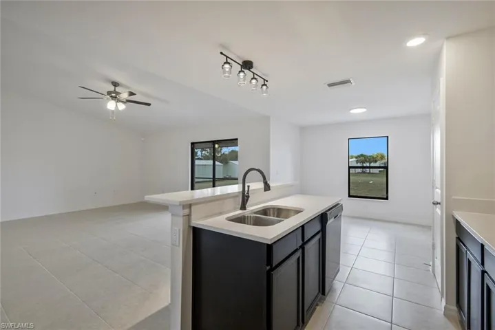 Kitchen featuring dark cabinetry, open floor plan, an island with sink, light tile patterned floors, and dishwasher