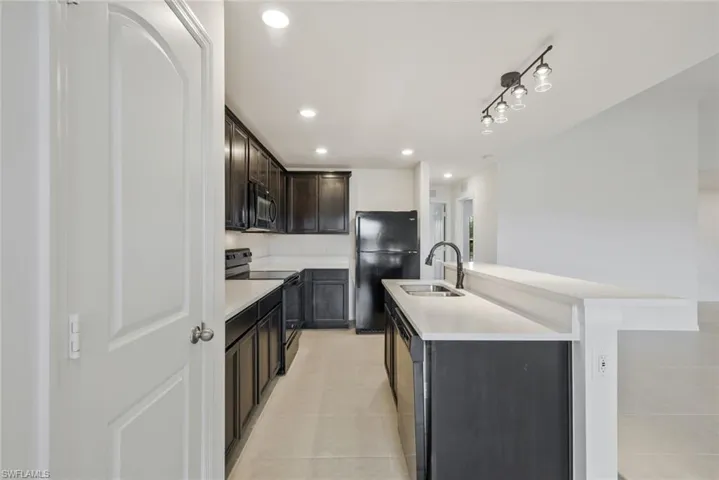 Kitchen featuring a kitchen island with sink, black appliances, recessed lighting, light tile patterned floors, and dark wood finish cabinetry