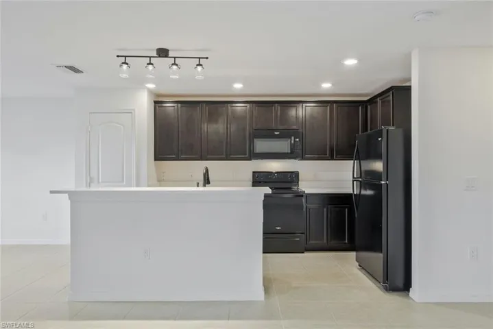 Kitchen featuring black appliances, dark wood finish cabinets, light countertops, a kitchen island, and light tile patterned flooring