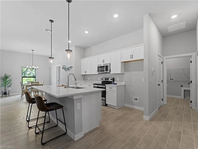 Kitchen featuring a kitchen breakfast bar, appliances with stainless steel finishes, an island with sink, decorative light fixtures, and sink