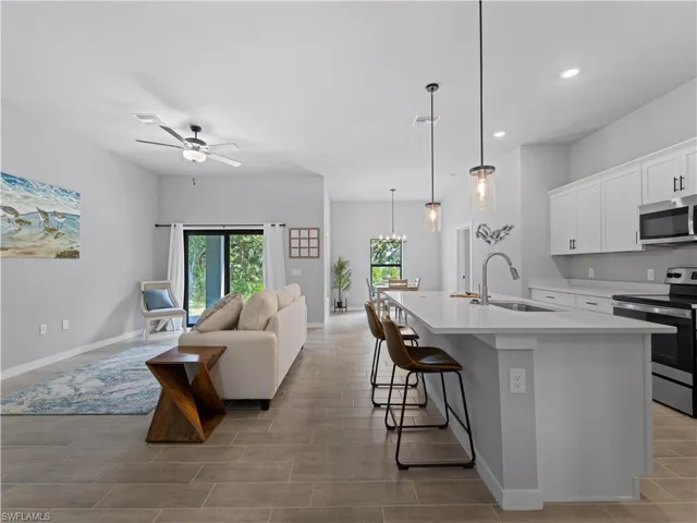 Kitchen with ceiling fan with notable chandelier, hanging light fixtures, a kitchen island with sink, appliances with stainless steel finishes, and sink