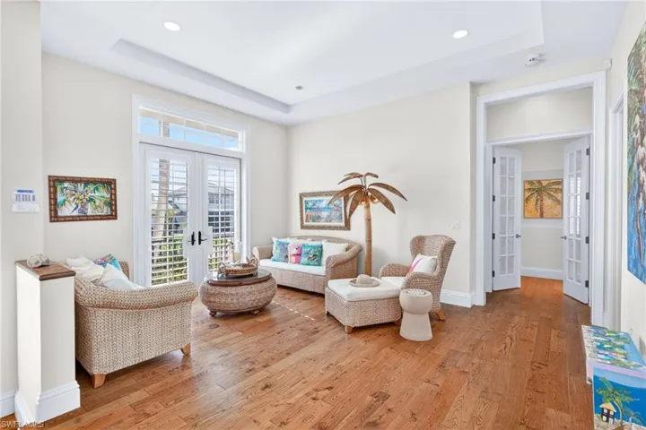 Living room with french doors, light wood finished floors, a raised ceiling, and recessed lighting