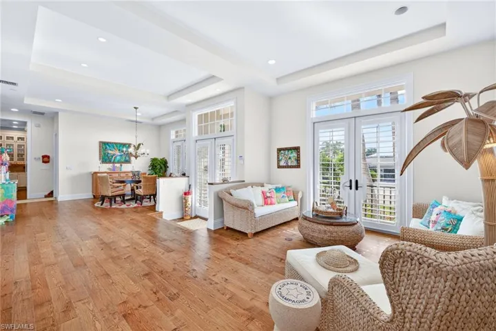 Living area with a raised ceiling, french doors, wood finished floors, recessed lighting, and a chandelier
