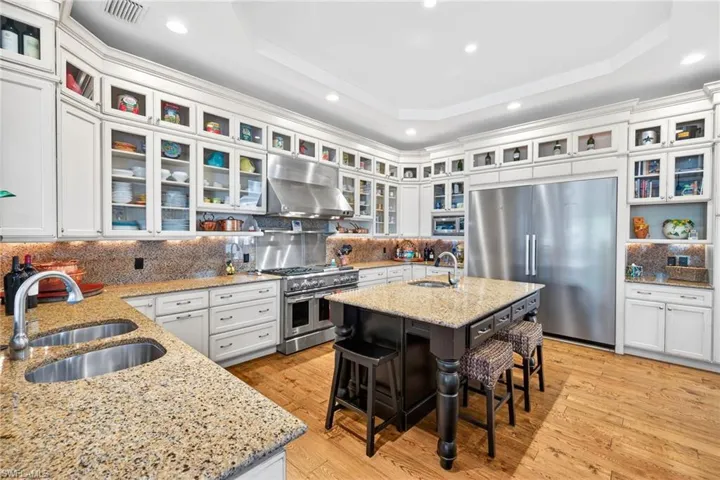Kitchen featuring built in appliances, white cabinets, light stone countertops, under cabinet range hood, and decorative backsplash