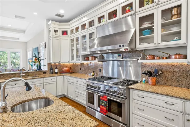 Kitchen with under cabinet range hood, range with two ovens, white cabinets, light stone counters, and recessed lighting