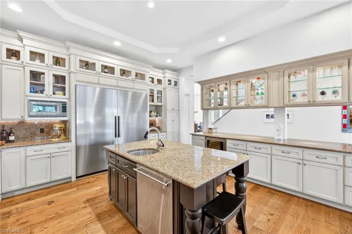 Kitchen with built in appliances, light stone counters, recessed lighting, a center island with sink, and glass insert cabinets