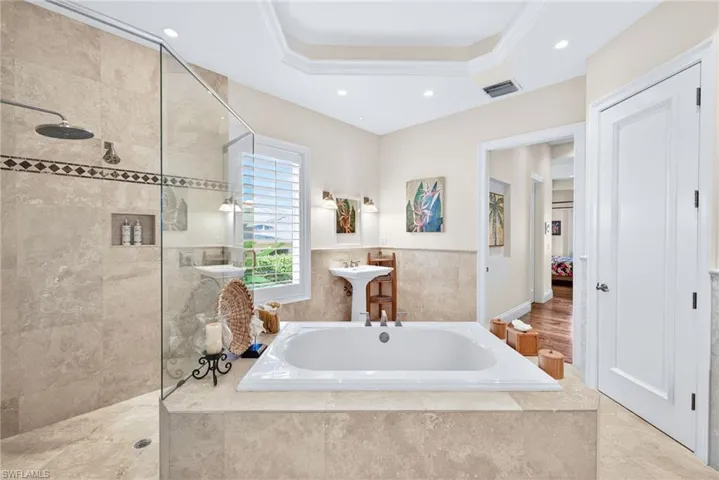 Bathroom featuring a bath, a tray ceiling, a walk in shower, recessed lighting, and ensuite bath