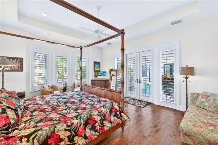 Bedroom with a raised ceiling, french doors, wood-type flooring, access to exterior, and multiple windows