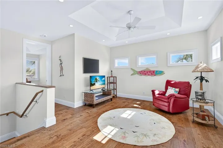 Living area with an upstairs landing, a tray ceiling, hardwood / wood-style flooring, and recessed lighting