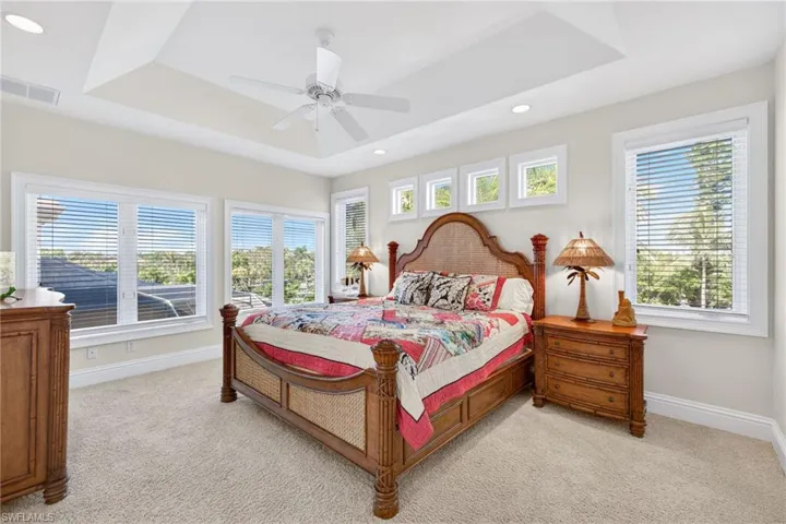 Bedroom featuring a ceiling fan, light colored carpet, a raised ceiling, multiple windows, and recessed lighting