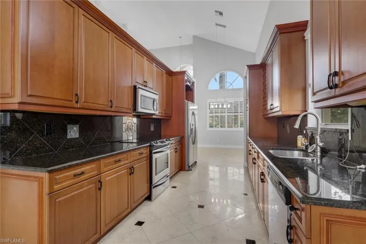 Kitchen featuring vaulted ceiling, stainless steel appliances, dark stone counters, wood finish cabinets, and light tile patterned flooring