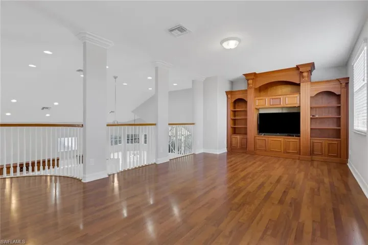 Unfurnished living room featuring dark wood-style floors, recessed lighting, and ornate columns