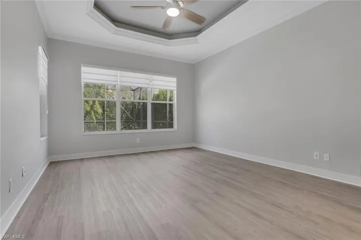 Spare room featuring a tray ceiling, ceiling fan, light wood finished floors, and ornamental molding