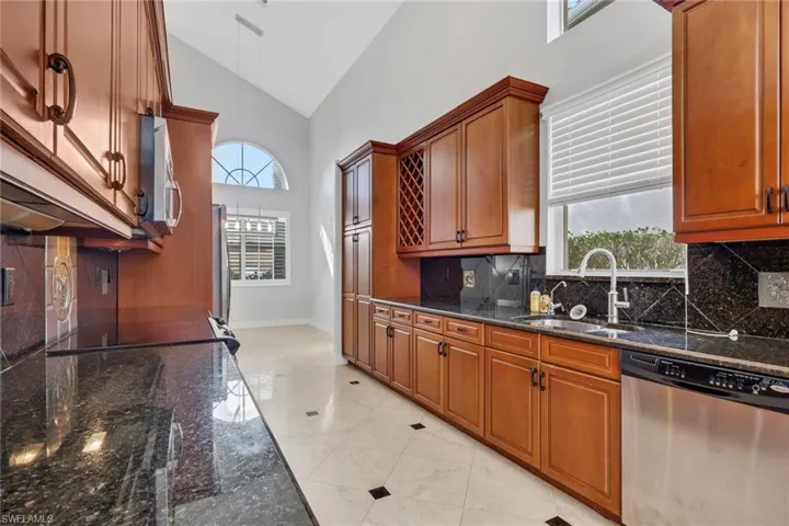 Kitchen featuring dark stone counters, stainless steel appliances, lofted ceiling, healthy amount of natural light, and wood finish cabinets
