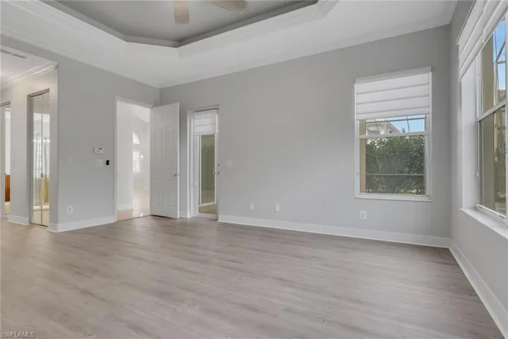 Empty room featuring crown molding, a ceiling fan, light wood-style floors, and a tray ceiling