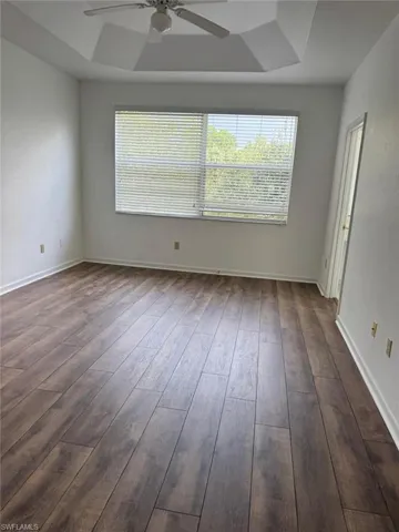 Spacious room featuring wood-finish flooring, a tray ceiling, and a ceiling fan with integrated lighting