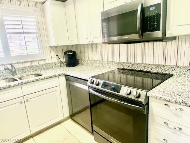 Kitchen featuring light stone counters, light tile patterned floors, white cabinets, stainless steel appliances, and a sink