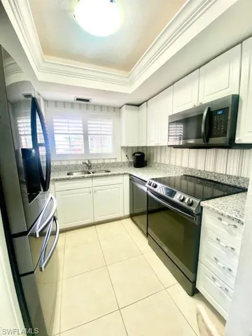 Kitchen featuring ornamental molding, light tile patterned floors, a tray ceiling, appliances with stainless steel finishes, and a sink