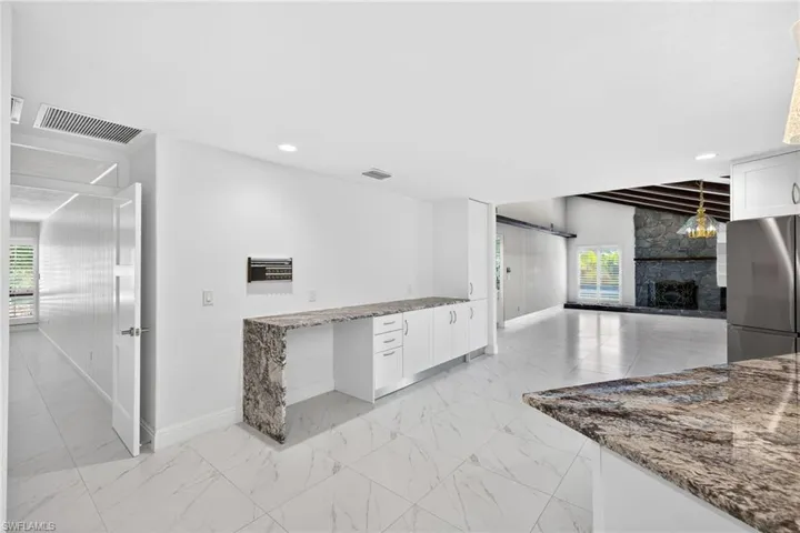 Kitchen with dark stone counters, white cabinets, a stone fireplace, freestanding refrigerator, and open floor plan