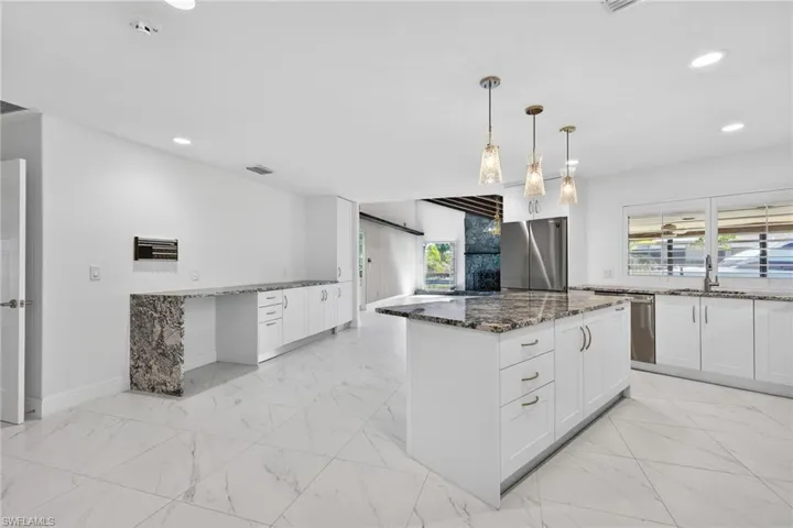 Kitchen with dark stone countertops, light marble finish floors, and a kitchen island