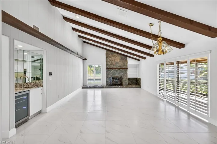 Unfurnished living room with wine cooler, vaulted ceiling, a stone fireplace, light marble finish flooring, and bar