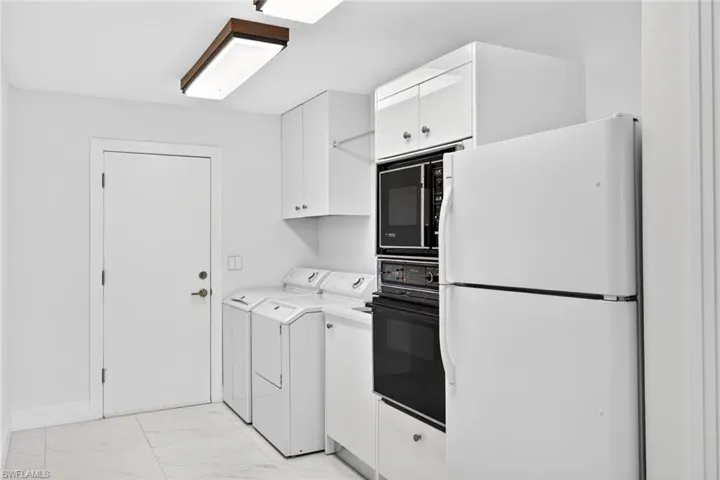 Kitchen featuring black appliances, white cabinets, light countertops, light marble finish flooring, and separate washer and dryer