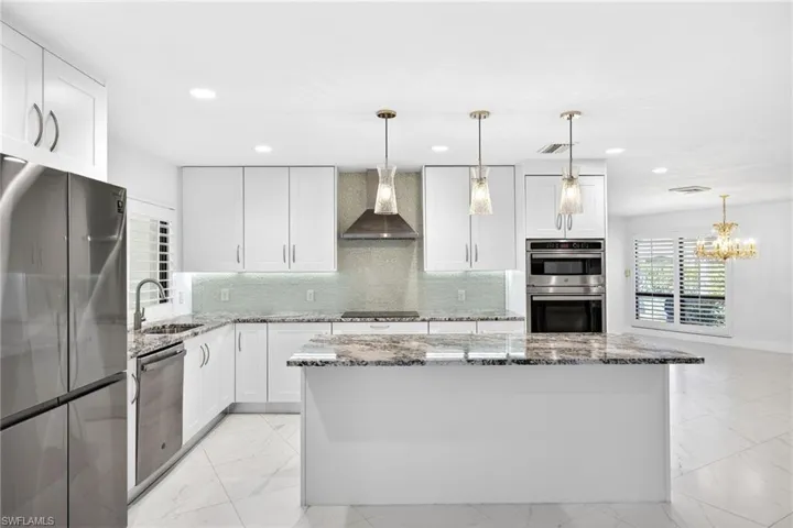 Kitchen featuring dark stone counters, stainless steel appliances, tasteful backsplash, and white cabinetry