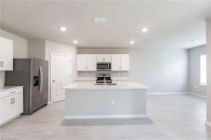 Kitchen with light wood-type flooring, a center island with sink, stainless steel appliances, white cabinets, and sink
