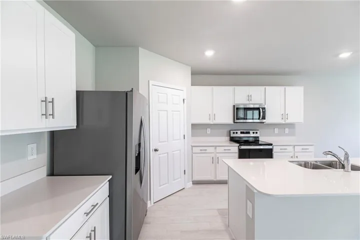 Kitchen featuring light hardwood / wood-style flooring, a center island with sink, sink, white cabinets, and appliances with stainless steel finishes