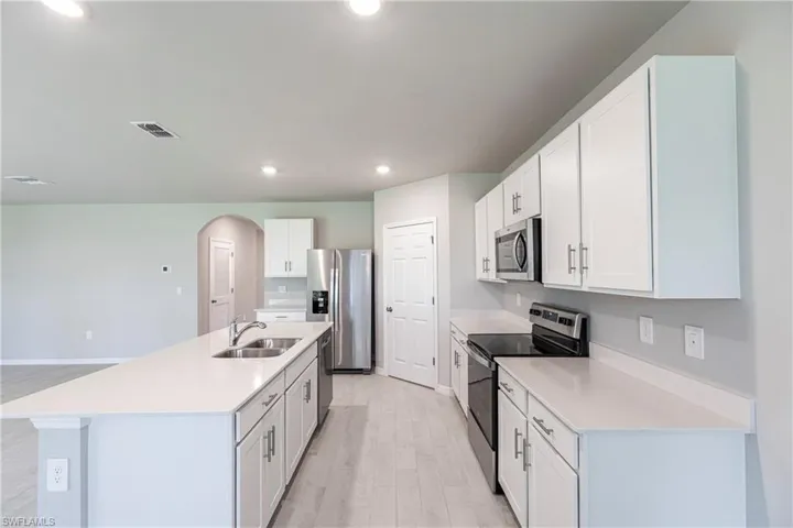 Kitchen with light hardwood / wood-style floors, a center island with sink, sink, white cabinets, and appliances with stainless steel finishes