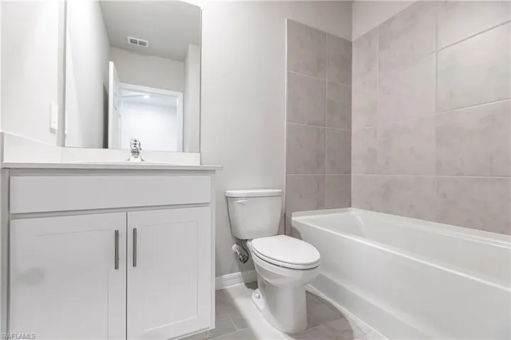 Full bathroom with tile flooring, toilet, tiled shower / bath combo, and large vanity