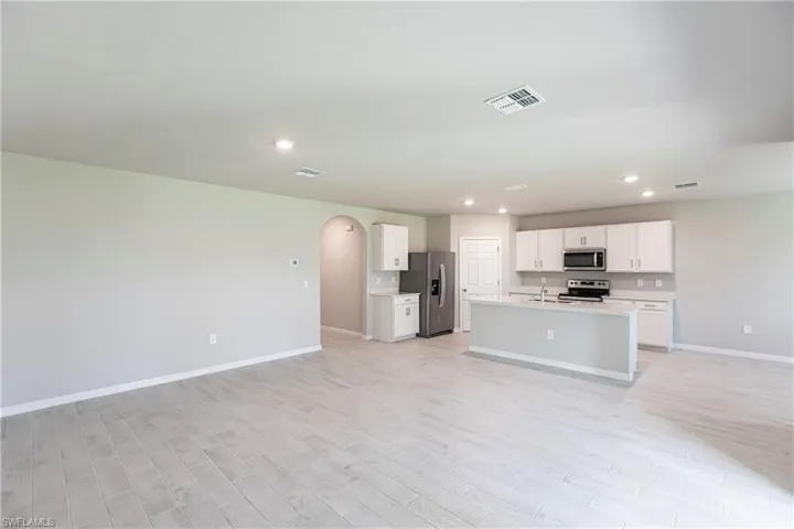 Kitchen featuring appliances with stainless steel finishes, white cabinetry, a kitchen island with sink, and light wood-type flooring
