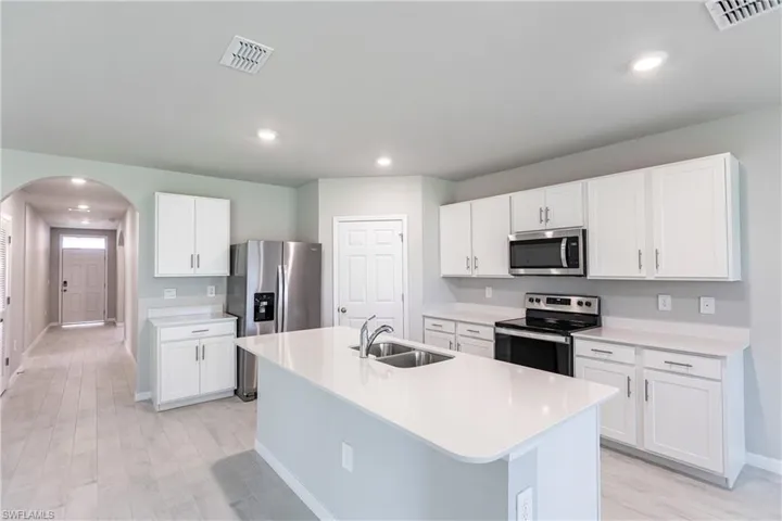 Kitchen with stainless steel appliances, sink, white cabinets, and a kitchen island with sink