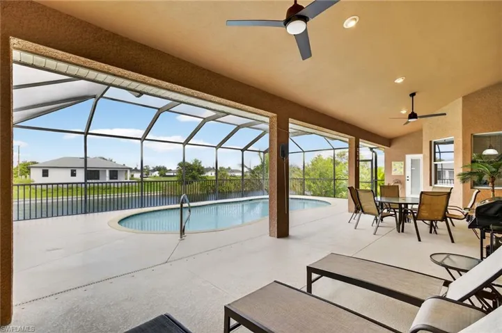 View of pool with a ceiling fan, a patio, outdoor dining area, and glass enclosure
